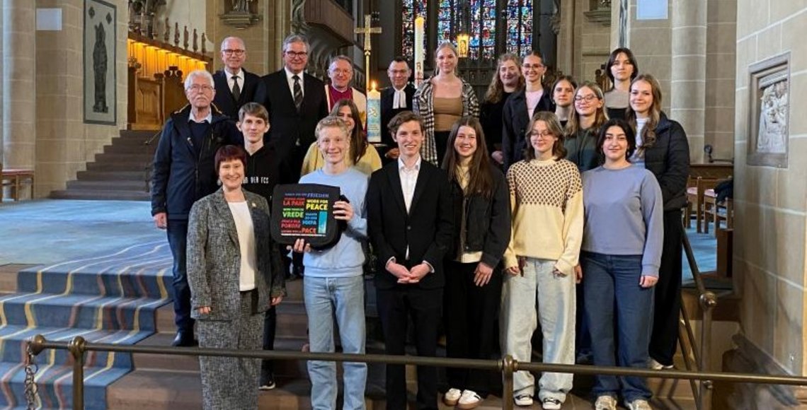 Das Foto zeigt die handelnden Akteure vor der Friedenskerze nach dem Gottesdienst im Altarraum des Domes zu Paderborn. Die Schülerinnen und Schüler des Gymnasiums St. Michael mit ihrer Lehrerin Manuela Lüftner, Christine Bentler (2. Stellv. Vorsitzende des Kreisverbandes Paderborn im Volksbund), Hermann-Josef Bentler (Mitglied des Kreisvorstandes Paderborn im Volksbund), Manfred Müller (Landrat a.D. und ehemaliger Vorsitzender des Kreisverbandes Paderborn im Volksbund), Bürgermeister Michael Dreier, Dechant Benedikt Fischer und Pfarrer Dr. Eckhard Düker ( v.u. nach o.).