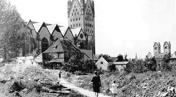 Das Foto von 1949 zeigt im Vordergrund eine Mutter mit Kind, die durch das durch den Zweiten Weltkrieg massiv zerstörte Paderborn auf den Dom zuläuft, der ebenfalls zum Teil zerstört wurde. 